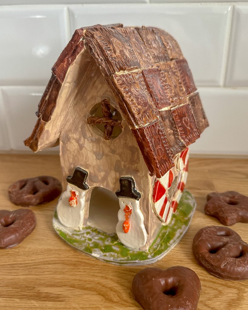 Ein Knusperhäuschen aus Ton. Drumherum liegen Lebkuchen.