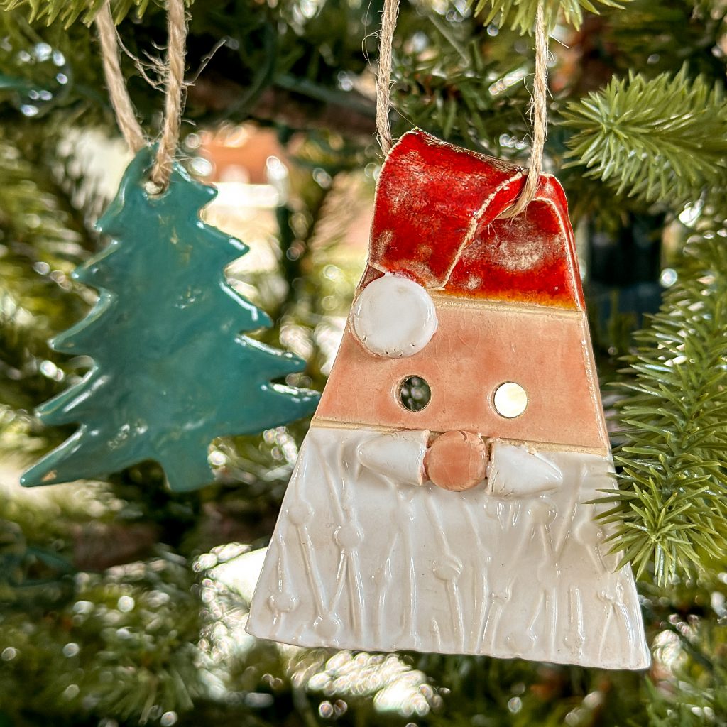 Ein grüner Tannenbaum-Anhänger und eine Weihnachtsmann-Anhänger hängen an einem Tannenbaum.